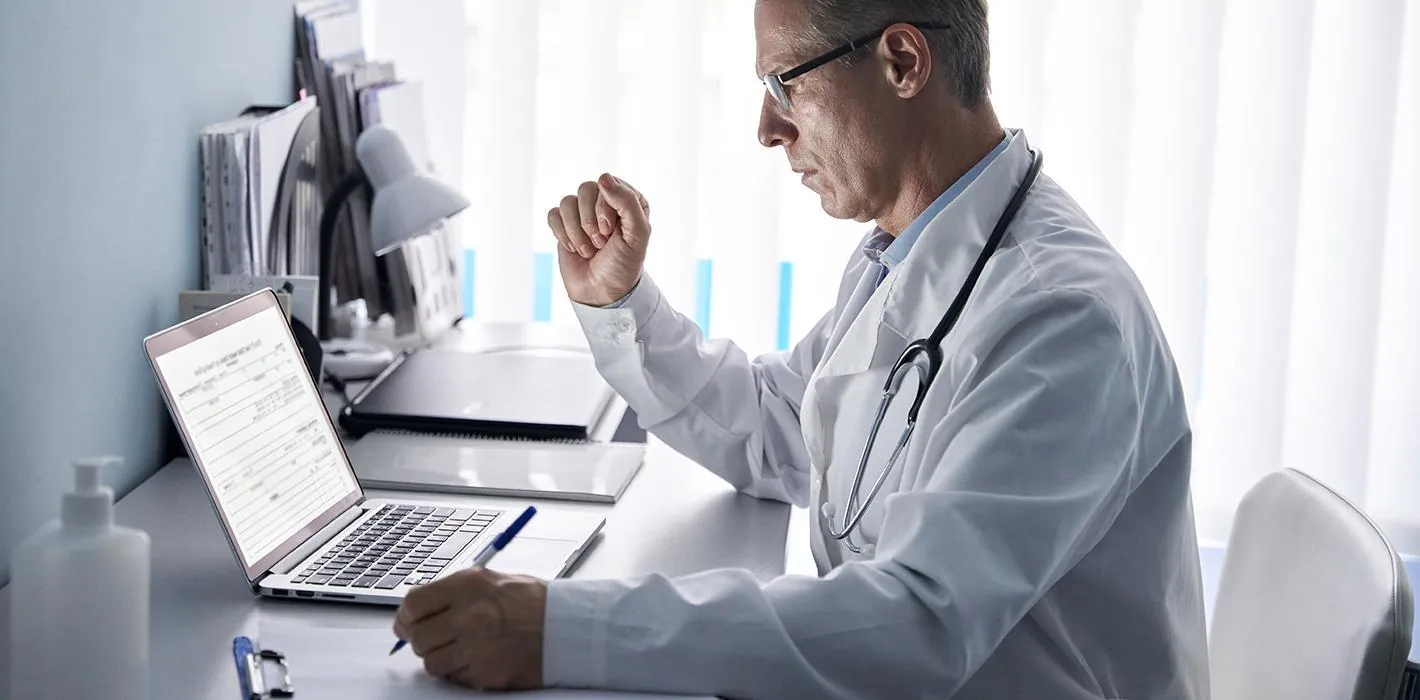 A physician talking with a patient across a desk in a calm clinical office.